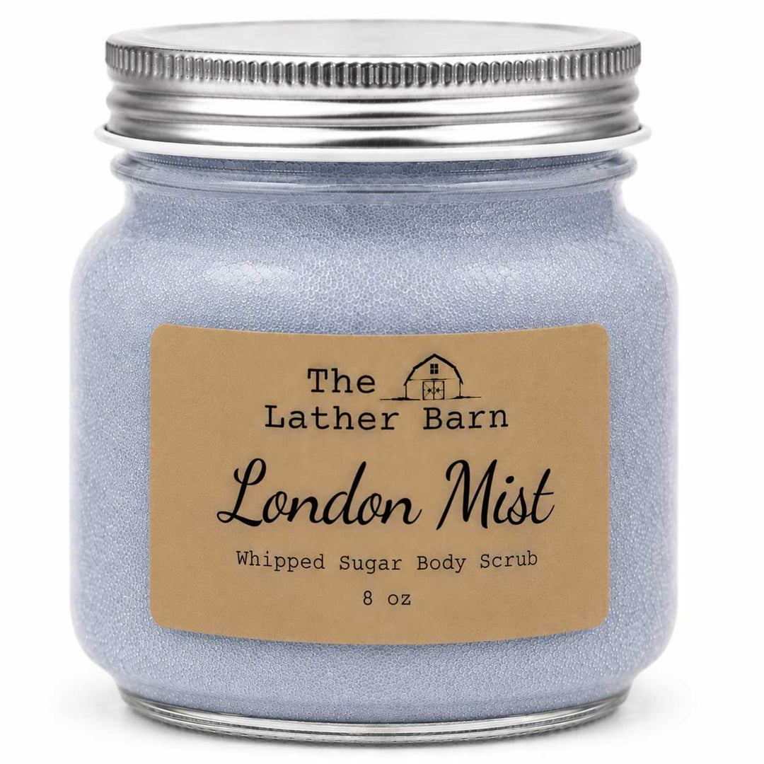 A 8 oz glass jar candle or body scrub by The Lather Barn, filled with a light lavender-blue whipped sugar scrub, featuring a kraft paper label and a silver metal screw-on lid.