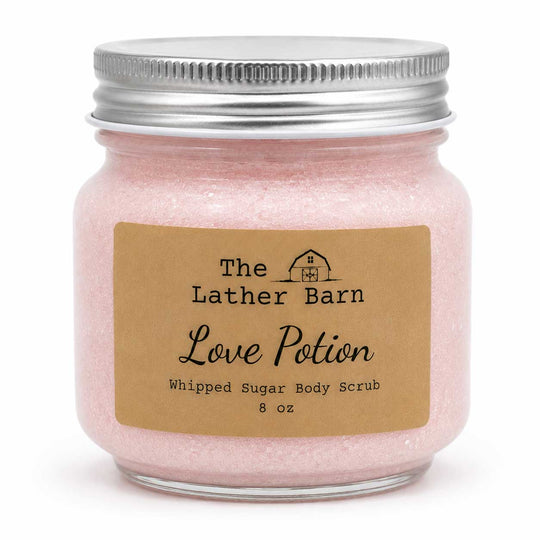 A 8 oz jar of The Lather Barn Love Potion Whipped Sugar Body Scrub, filled with light pink scrub and featuring a brown kraft paper label and a silver metal lid, set against a plain white background.