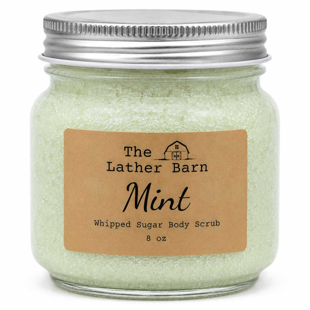 A 8 oz glass jar of The Lather Barn Mint Whipped Sugar Body Scrub, filled with pale mint green scrub and sealed with a silver metal lid, featuring a brown kraft paper label.