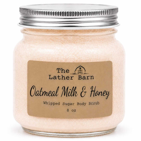 A 8 oz jar of 'The Lather Barn' Oatmeal Milk & Honey Whipped Sugar Body Scrub. The product is shown in a clear glass jar filled with a light beige, shimmering scrub, topped with a silver metal screw lid and featuring a brown kraft paper label.