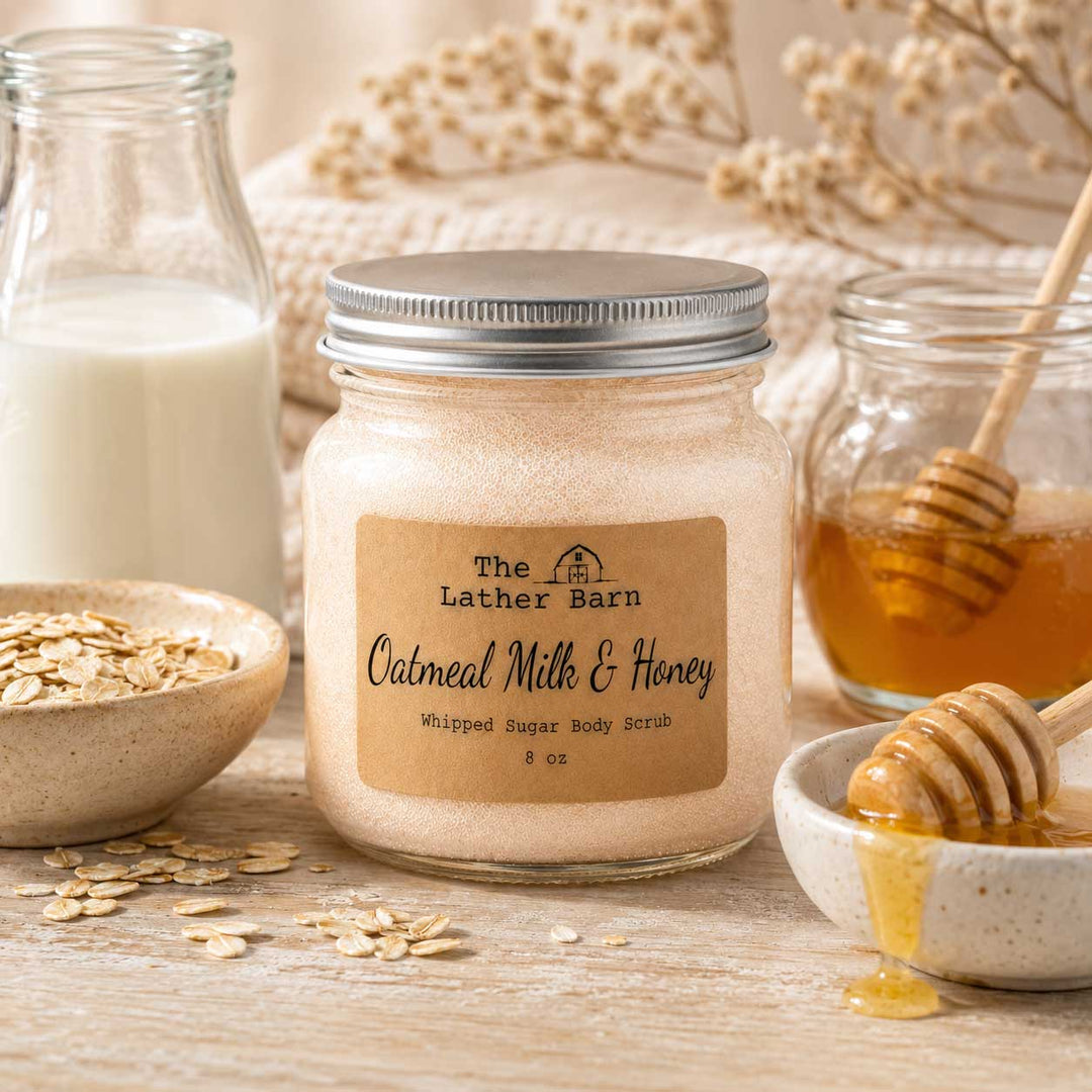 A jar of oatmeal milk and honey whipped sugar body scrub by The Lather Barn, styled on a rustic wooden surface with oats, a glass bottle of milk, honey, and a honey dipper.