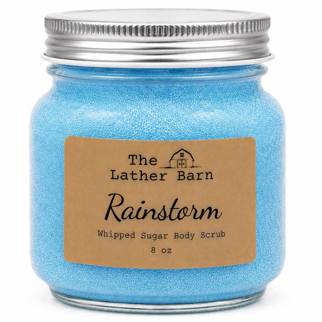 A 8 oz jar of The Lather Barn Rainstorm Whipped Sugar Body Scrub, filled with light blue scrub and featuring a brown kraft paper label and a silver metal screw cap, shown on a white background.