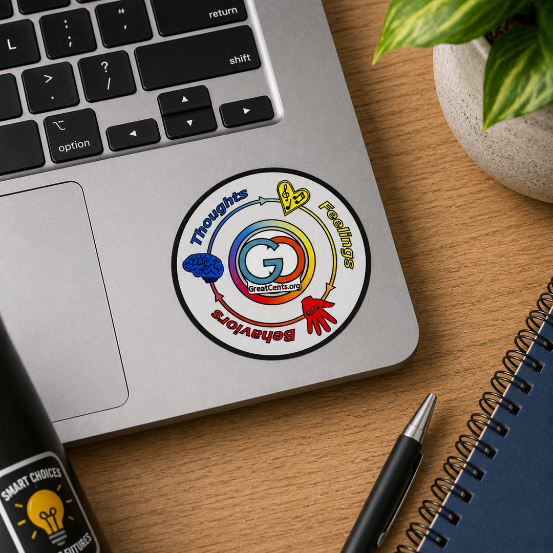 A round sticker with a colorful rainbow and the letter G, placed on the palm rest of a silver laptop on a wooden desk. The sticker includes the words 'Thoughts Feelings Behaviors' and a small 'GreatChoices' logo.