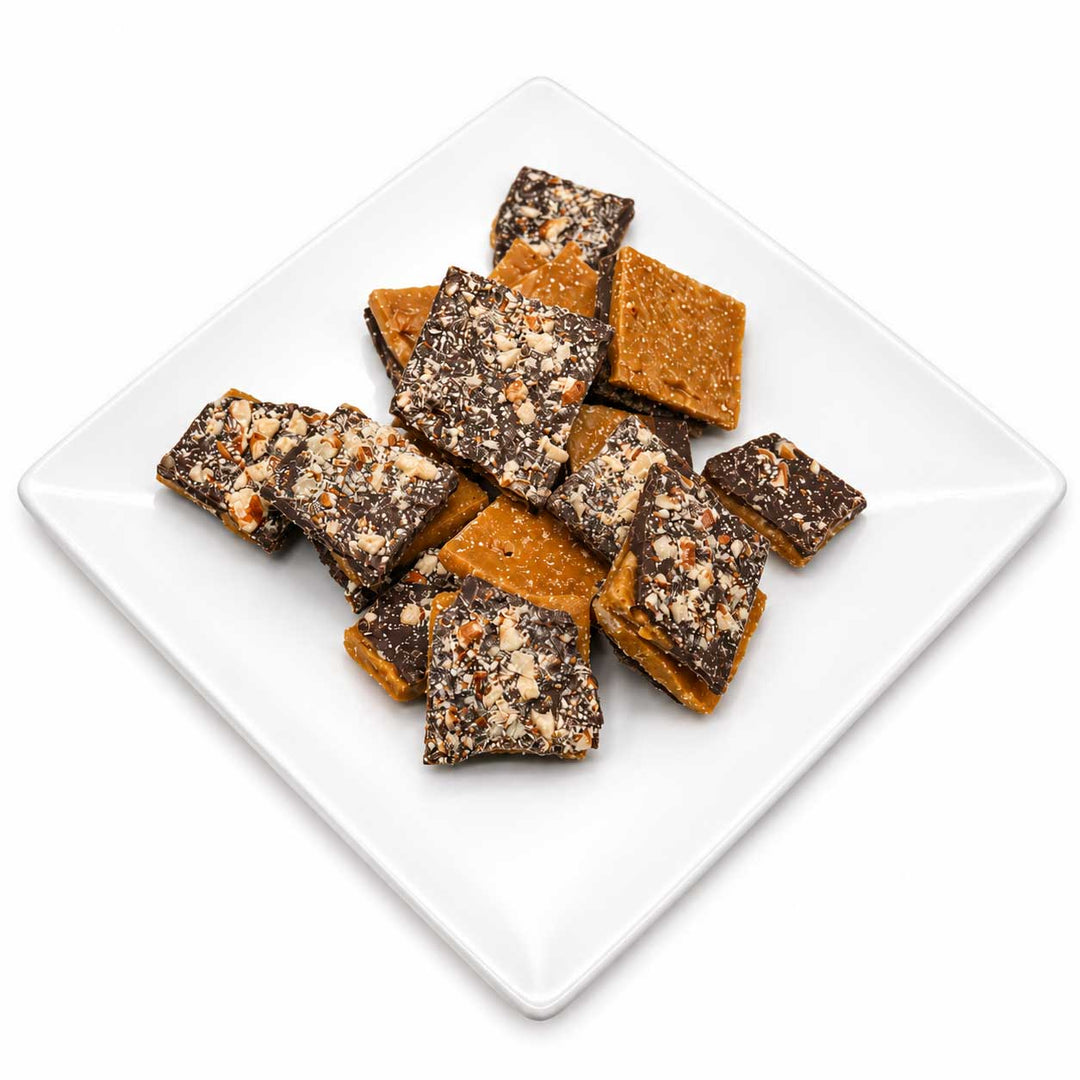 A pile of square chocolate-dipped nuts or candy bars with chopped nuts on top, served on a white square plate against a white background.