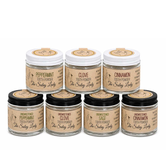 Set of seven jars of 'The Salty Lady' tooth powder with different flavors on a white background.