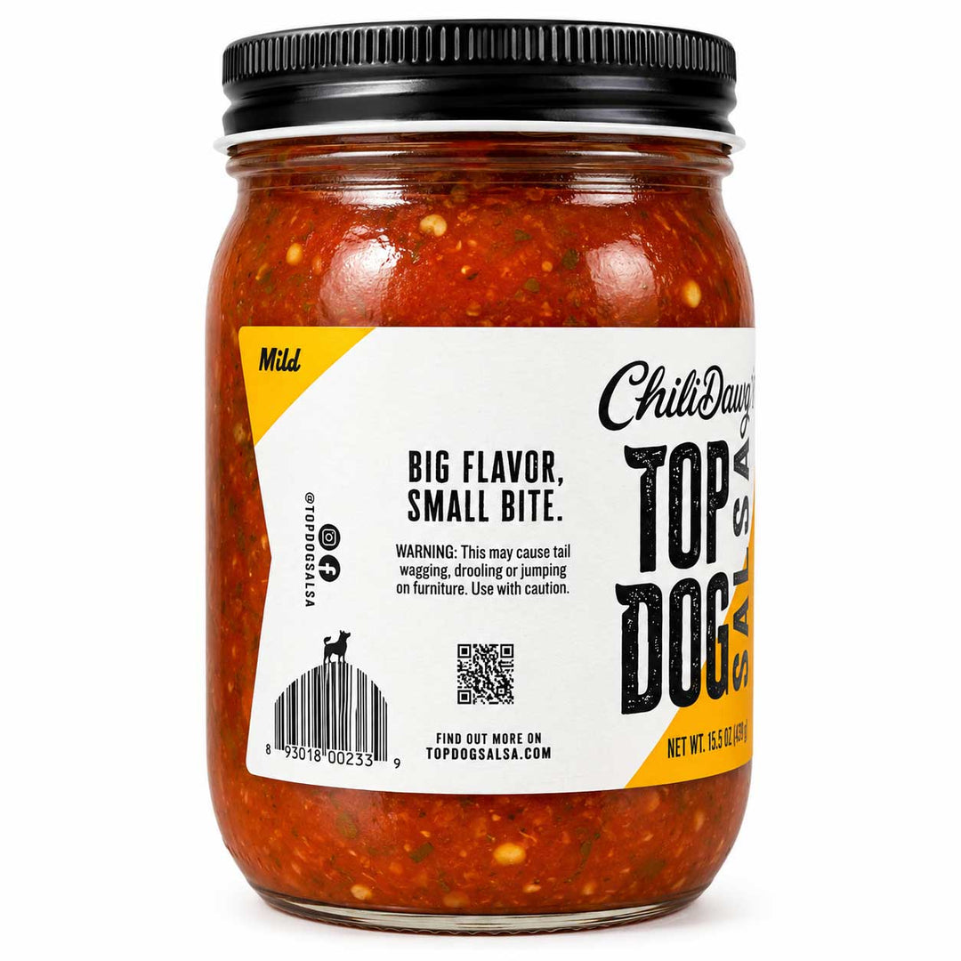A glass jar of Top of the Dog Chili Dog food, featuring a white and yellow label with black text, a black metal lid, and visible red chili sauce with flecks inside, set against a plain white background.