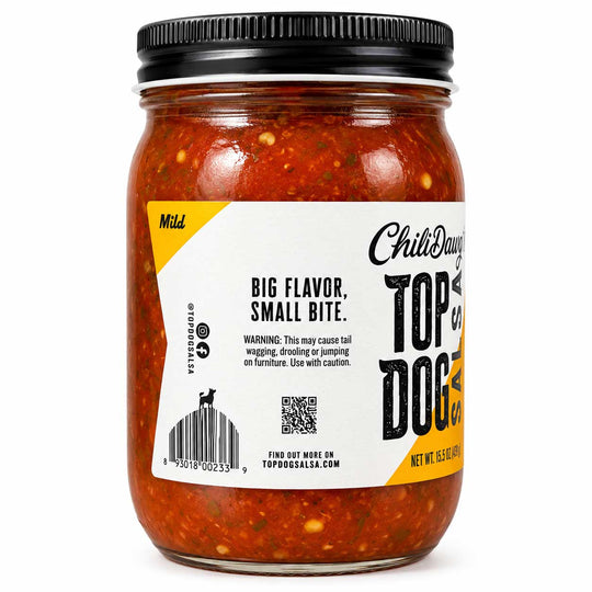 A glass jar of Top of the Dog Chili Dog food, featuring a white and yellow label with black text, a black metal lid, and visible red chili sauce with flecks inside, set against a plain white background.