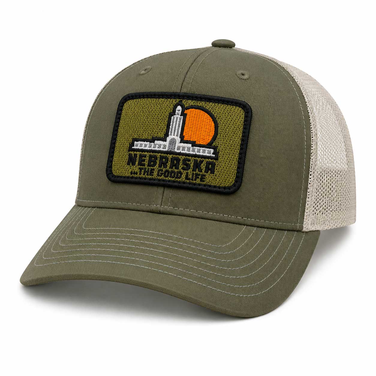 An olive green and beige trucker hat featuring a rectangular embroidered patch on the front with the Nebraska skyline and the text 'NEBRASKA WITH THE GOOD LIFE'.