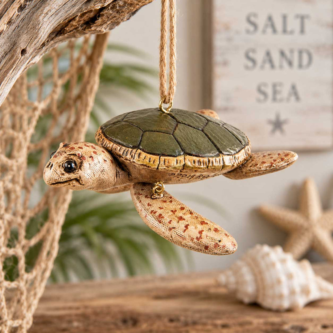 A sea turtle hanging ornament made to look like a real turtle, suspended by a rope. The ornament has a textured tan head and flippers with reddish-brown speckles and a dark olive-green shell.