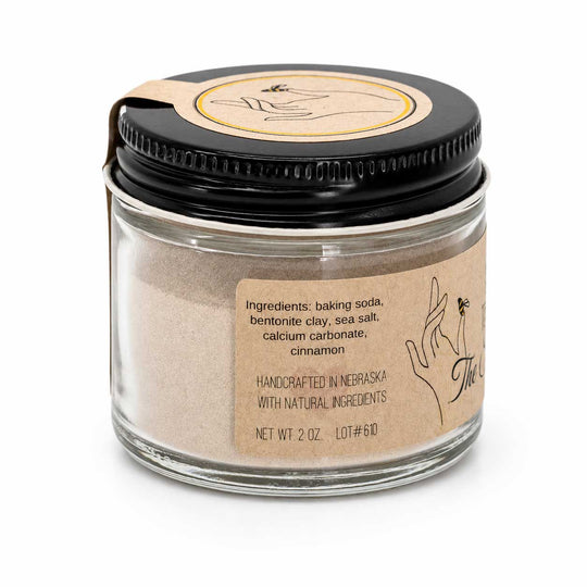 Glass jar with black lid containing a powder, labeled 'Handcrafted in Nebraska with Natural Ingredients'.