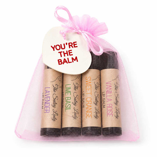 Set of lip balms in kraft paper packaging with a pink sheer bag and 'You're the Balm' tag.