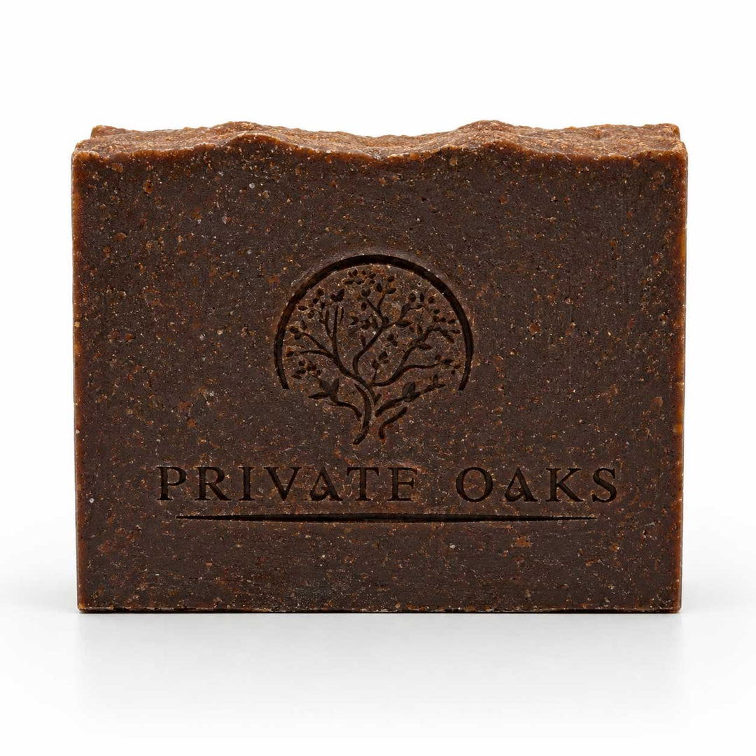 A rectangular bar of dark brown handmade soap with a textured surface, featuring an embossed tree logo and the brand name 'PRIVATE OAKS' on the front, set against a plain white background.