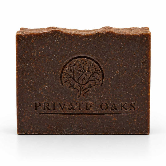 A rectangular bar of dark brown handmade soap with a textured surface, featuring an embossed tree logo and the brand name 'PRIVATE OAKS' on the front, set against a plain white background.