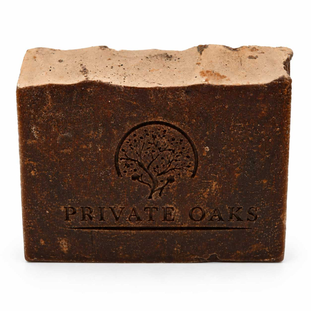 A rectangular bar of soap with a rustic, textured dark brown finish and a lighter beige top surface. The front is embossed with a tree logo and the brand name 'PRIVATE OAKS' in a serif font, set against a plain white background.