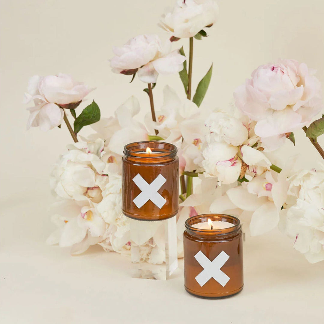 Two candles with 'X' symbols in front of white flowers on a light background