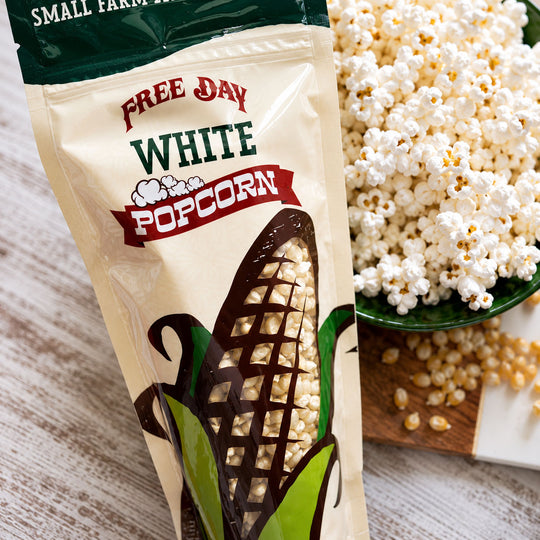 Free Day White Popcorn package with popcorn and kernels on a wooden surface