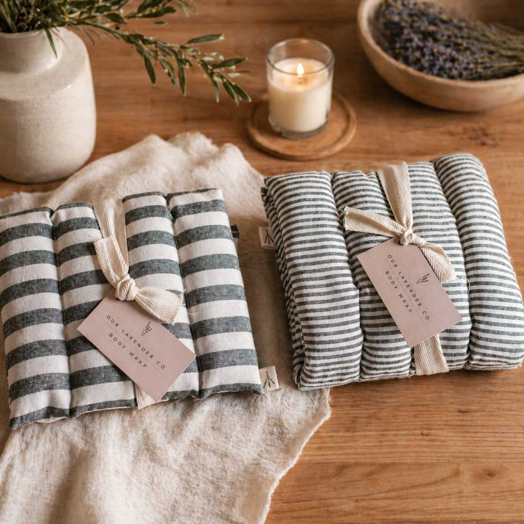 Two sets of striped products with tags on a wooden surface, surrounded by a candle and plants.