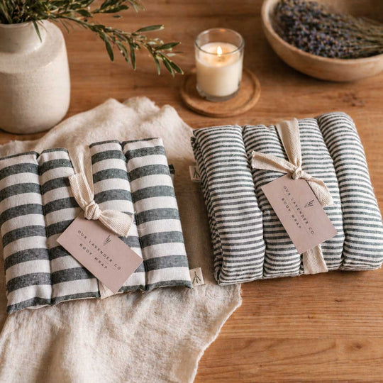 Two sets of striped products with tags on a wooden surface, surrounded by a candle and plants.