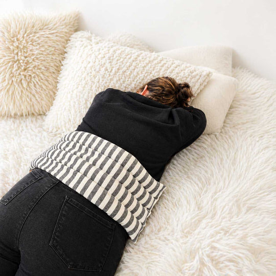 Person lying on a bed with white pillows and a striped blanket