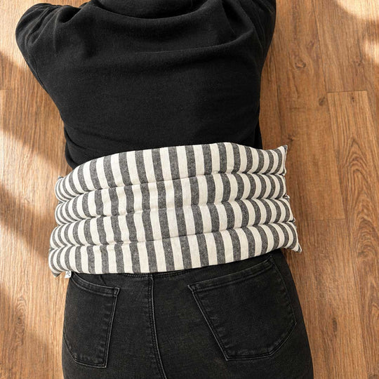 Person wearing a black sweater with a striped cushion over their stomach on a wooden floor.
