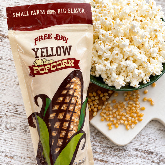 Free Day Yellow Popcorn package with a bowl of popcorn and kernels on a wooden surface
