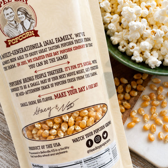 Popcorn bag with text and graphics, surrounded by popcorn kernels and a bowl of popcorn.