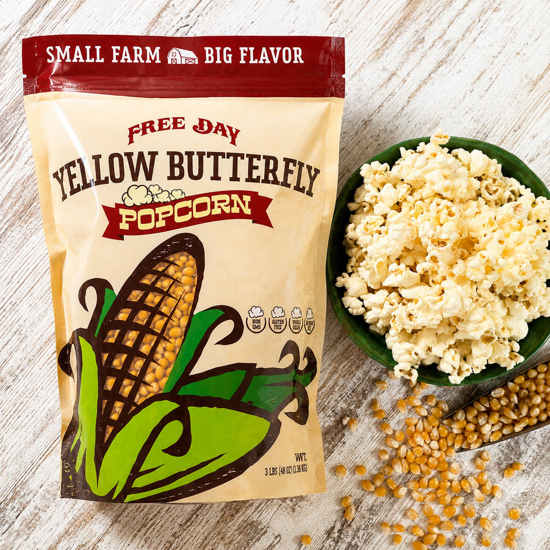 Free Day Yellow Butterfly Popcorn bag with a bowl of popcorn and spilled kernels on a wooden surface.