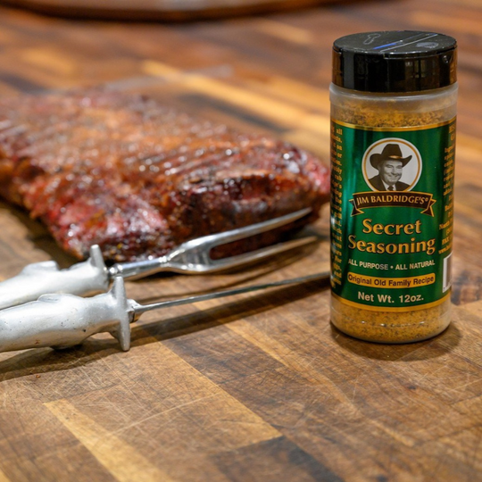 A Bottle Of Jim Baldridge Secret Seasoning Sitting Next To A Piece Of Cooked Meat 