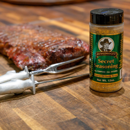 Jim Baldridge Secret Seasoning bottle sitting next to a piece of cooked meat. 