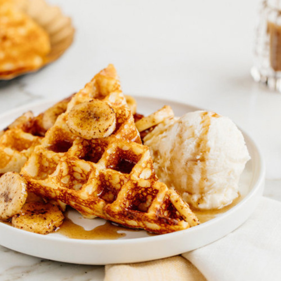 Plate of fresh waffles topped with syrup, sliced bananas, and a dollop of butter