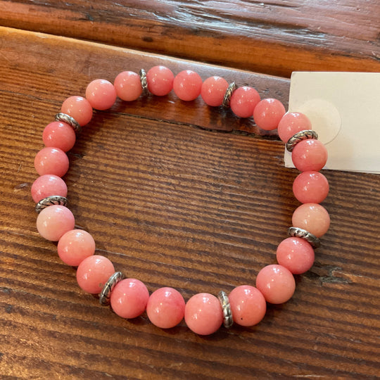 A pink beaded bracelet with metallic accents, displayed on a wooden surface.